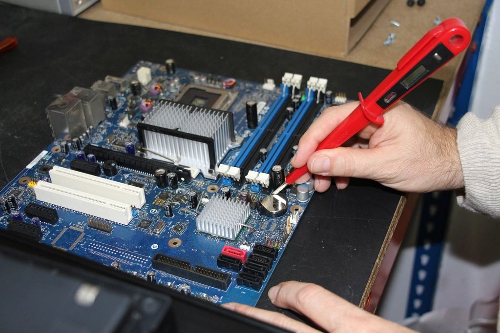 A hand working on a computer circuit board with a red screwdriver.