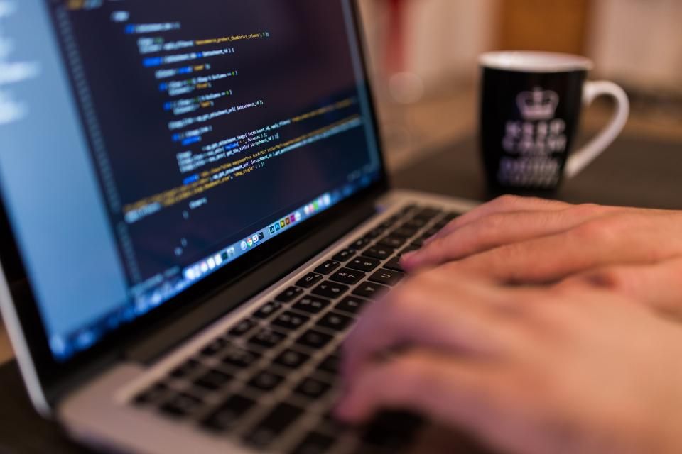 Hands typing on a laptop with code on the screen.