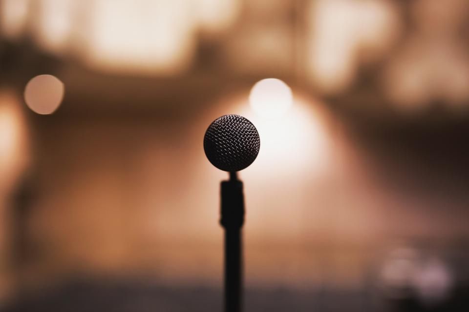 A microphone on a stand in front of warm, out-of-focus stage lights.